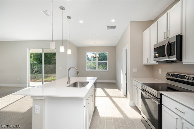 kitchen with an island with sink, pendant lighting, light hardwood / wood-style floors, appliances with stainless steel finishes, and sink