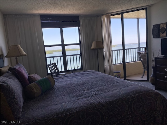 carpeted bedroom with a water view, a textured ceiling, and access to exterior