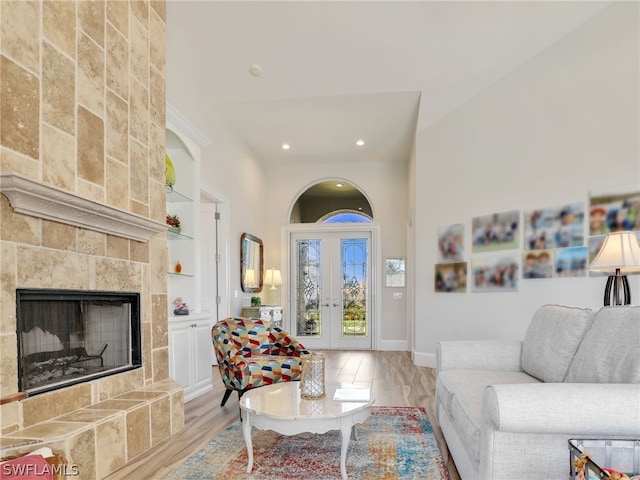 living room with built in shelves, light hardwood / wood-style floors, a tile fireplace, and french doors