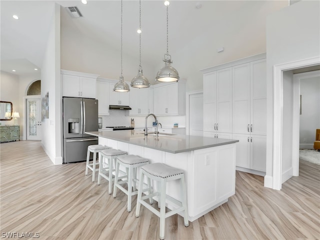 kitchen featuring an island with sink, stainless steel refrigerator with ice dispenser, high vaulted ceiling, and white cabinetry