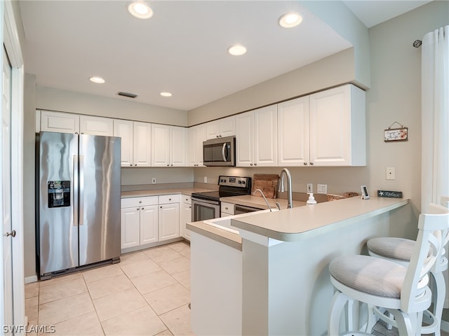 kitchen with a breakfast bar area, kitchen peninsula, stainless steel appliances, and white cabinets