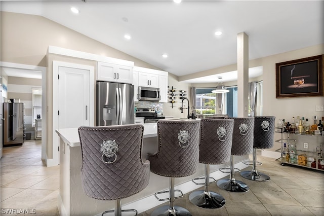 kitchen featuring vaulted ceiling, light tile patterned floors, a breakfast bar, white cabinetry, and appliances with stainless steel finishes