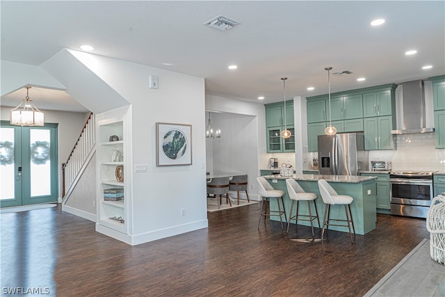 kitchen featuring a notable chandelier, wall chimney range hood, dark wood-type flooring, appliances with stainless steel finishes, and light stone counters