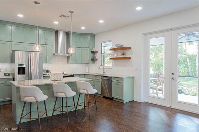 kitchen featuring pendant lighting, plenty of natural light, stainless steel appliances, dark wood-type flooring, and wall chimney exhaust hood