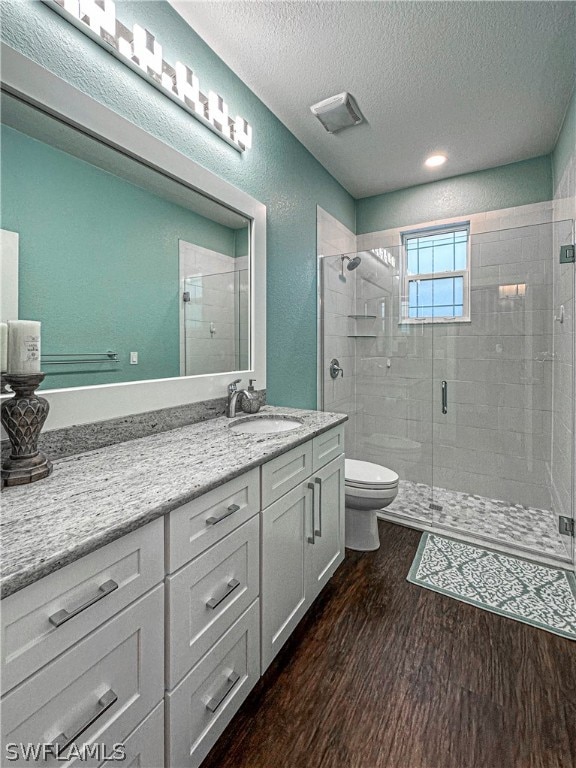 bathroom with toilet, a shower with shower door, vanity, hardwood / wood-style floors, and a textured ceiling