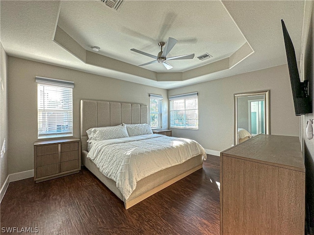 bedroom with dark hardwood / wood-style flooring, a tray ceiling, and multiple windows