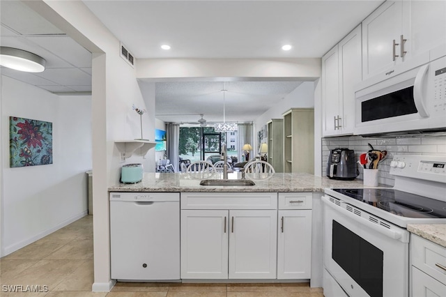 kitchen featuring white appliances, a sink, white cabinets, backsplash, and light stone countertops