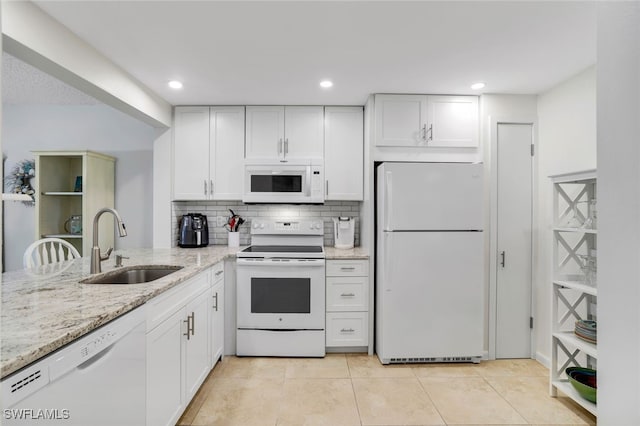 kitchen with white appliances, light tile patterned floors, white cabinets, light stone countertops, and a sink