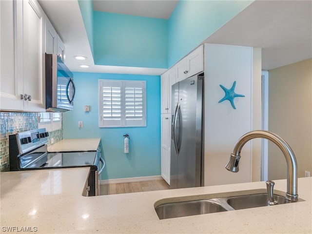 kitchen with white cabinets, a sink, light stone countertops, stainless steel appliances, and backsplash