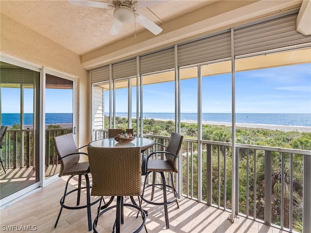 sunroom with a beach view, a water view, and a ceiling fan