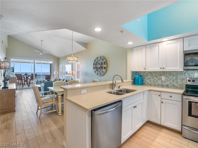 kitchen with appliances with stainless steel finishes, a peninsula, light countertops, white cabinetry, and a sink