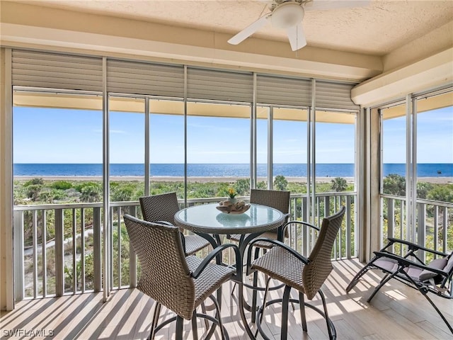 sunroom featuring a healthy amount of sunlight, a water view, ceiling fan, and a beach view