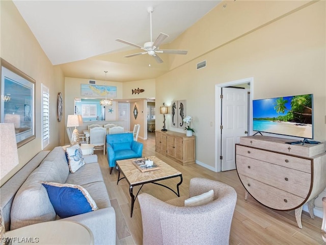 living area featuring light wood-style floors, visible vents, high vaulted ceiling, and ceiling fan with notable chandelier