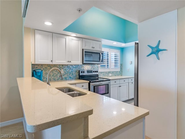 kitchen with a peninsula, a sink, white cabinets, appliances with stainless steel finishes, and decorative backsplash