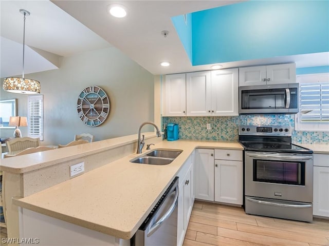 kitchen featuring backsplash, appliances with stainless steel finishes, light wood-style floors, a sink, and a peninsula