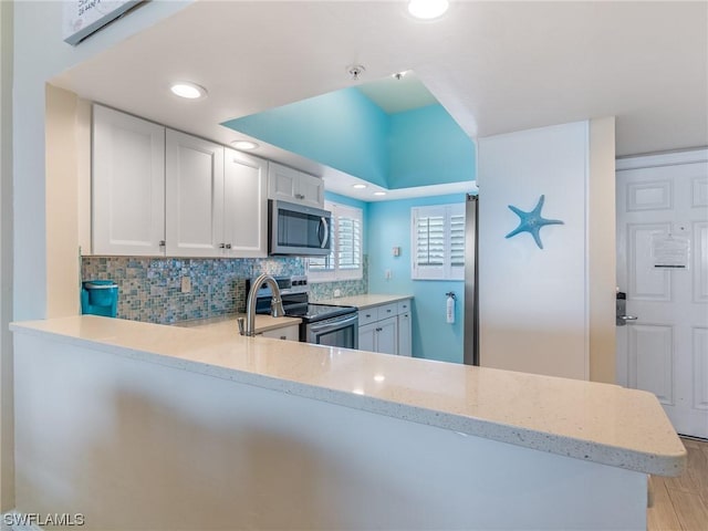 kitchen with tasteful backsplash, white cabinets, appliances with stainless steel finishes, light stone countertops, and light wood-style floors