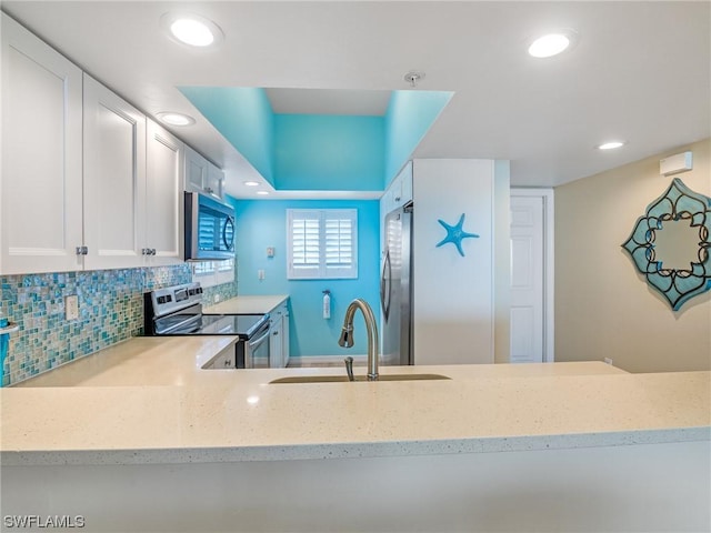 kitchen featuring white cabinets, decorative backsplash, appliances with stainless steel finishes, light stone countertops, and a sink