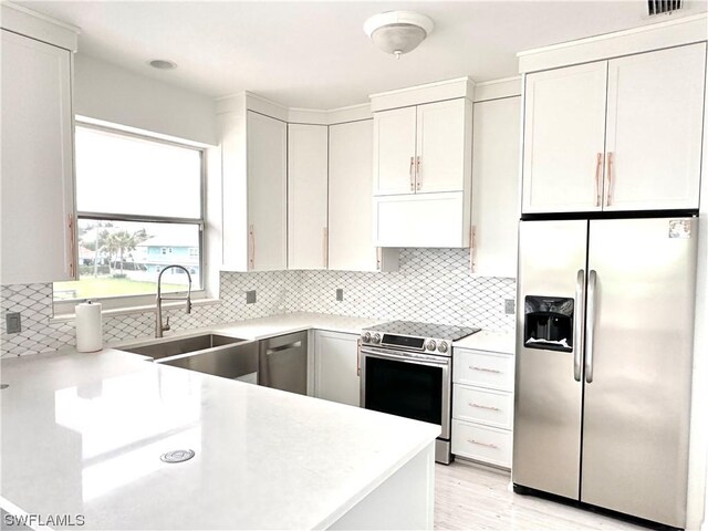 kitchen with backsplash, exhaust hood, white cabinets, sink, and appliances with stainless steel finishes