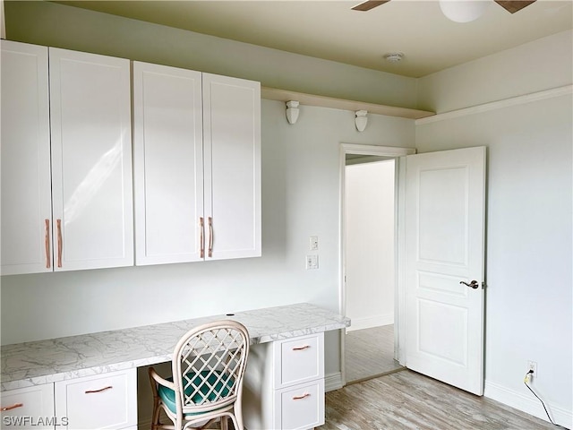 unfurnished office featuring light wood finished floors, built in study area, a ceiling fan, and baseboards