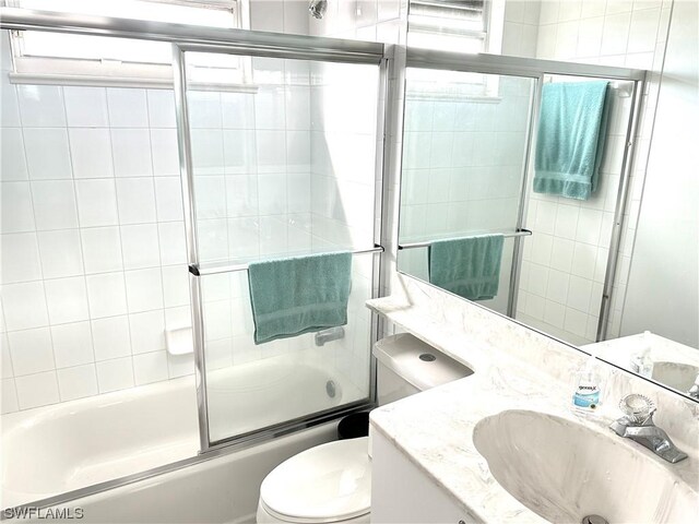 full bathroom with combined bath / shower with glass door, toilet, and vanity