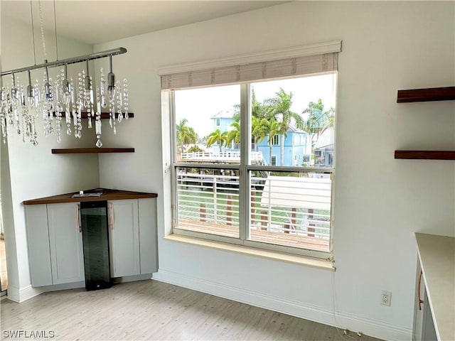 unfurnished dining area with beverage cooler, baseboards, and light wood-style floors