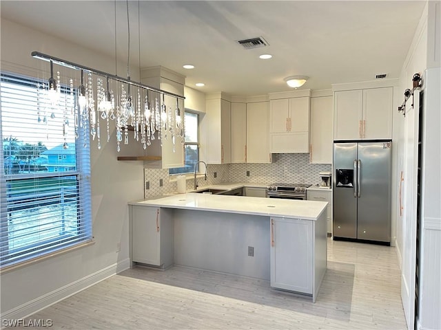 kitchen featuring visible vents, a peninsula, stainless steel appliances, light countertops, and a sink