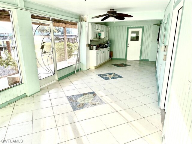 doorway featuring ceiling fan, light tile patterned floors, and wooden walls