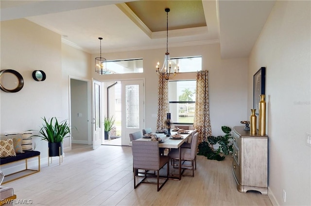 dining room with a notable chandelier, a raised ceiling, and light wood-type flooring