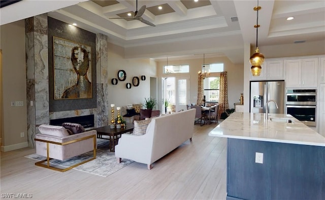 living room with coffered ceiling, ceiling fan with notable chandelier, sink, light hardwood / wood-style flooring, and a high end fireplace