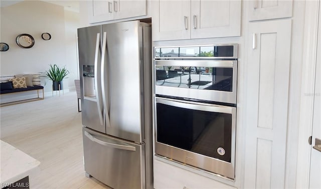 kitchen featuring white cabinets, light hardwood / wood-style flooring, light stone countertops, and stainless steel appliances