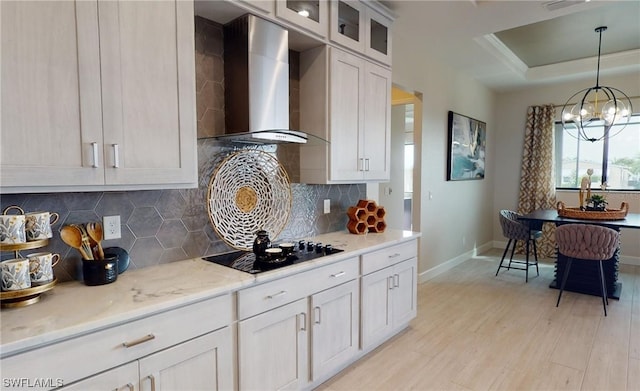 kitchen with white cabinets, a chandelier, backsplash, wall chimney exhaust hood, and light wood-type flooring