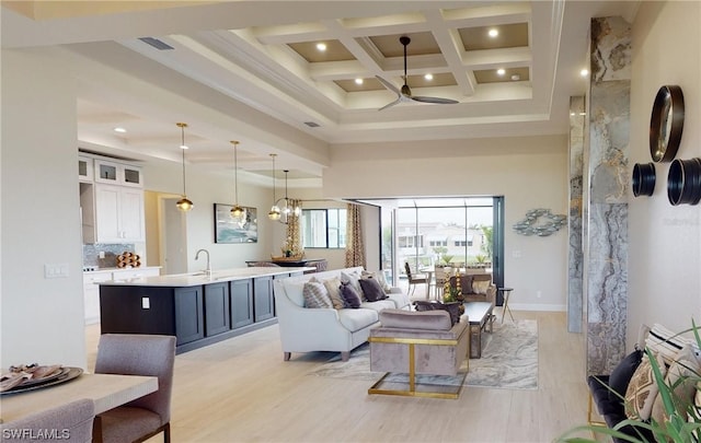 living room with a high ceiling, coffered ceiling, ceiling fan with notable chandelier, beamed ceiling, and crown molding