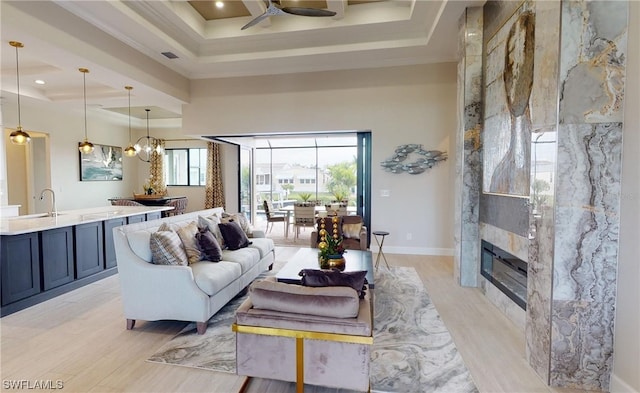 living room with ceiling fan with notable chandelier, sink, a tray ceiling, and light wood-type flooring