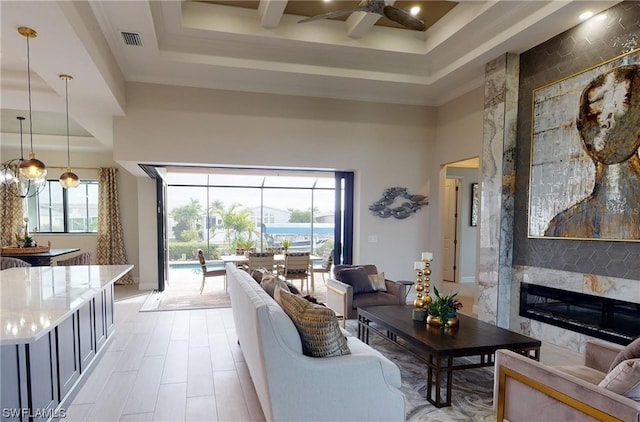 living room with a wealth of natural light, a raised ceiling, a large fireplace, and ceiling fan with notable chandelier