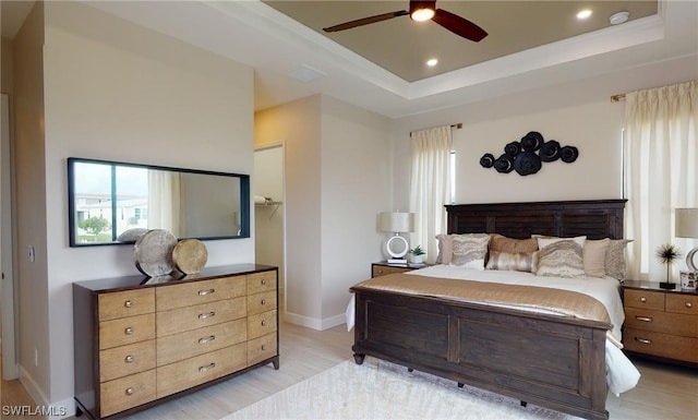 bedroom with a tray ceiling, ceiling fan, and light wood-type flooring