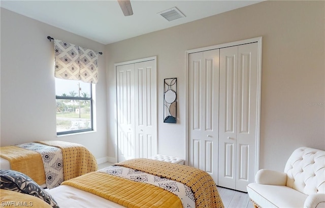 bedroom with ceiling fan, light hardwood / wood-style floors, and multiple closets