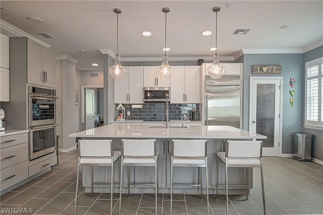 kitchen featuring hanging light fixtures, appliances with stainless steel finishes, dark tile patterned floors, and a kitchen island with sink