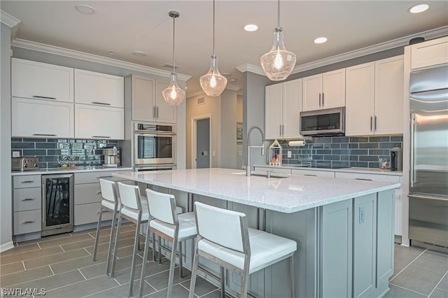 kitchen with light stone countertops, hanging light fixtures, stainless steel appliances, wine cooler, and a center island with sink