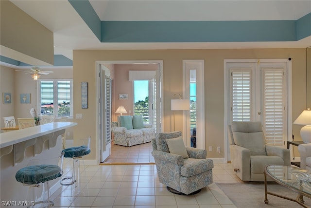 tiled living room with ceiling fan and a tray ceiling