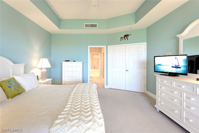 bedroom with a raised ceiling, light colored carpet, and a closet