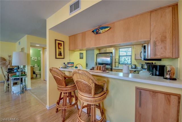 kitchen featuring light brown cabinetry, light hardwood / wood-style flooring, appliances with stainless steel finishes, and a breakfast bar