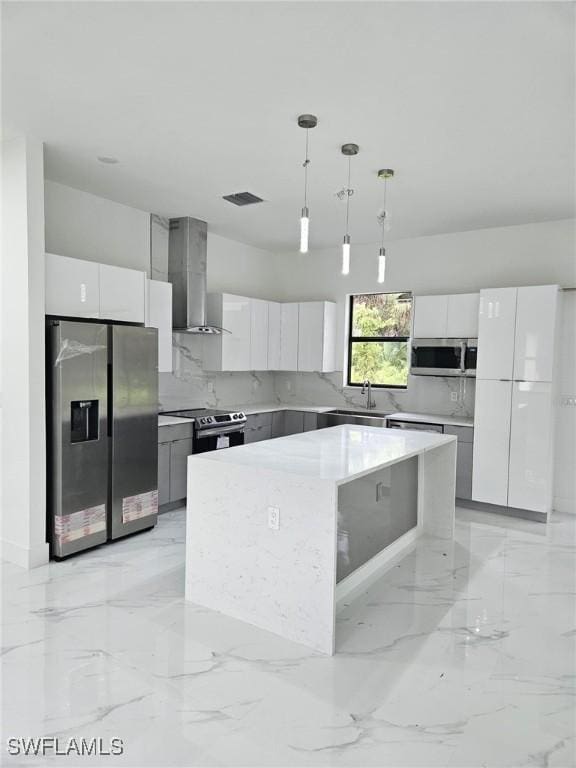 kitchen featuring white cabinetry, wall chimney range hood, decorative light fixtures, a kitchen island, and appliances with stainless steel finishes