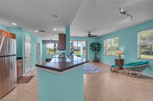 kitchen featuring ceiling fan, light tile patterned flooring, sink, kitchen peninsula, and stainless steel refrigerator