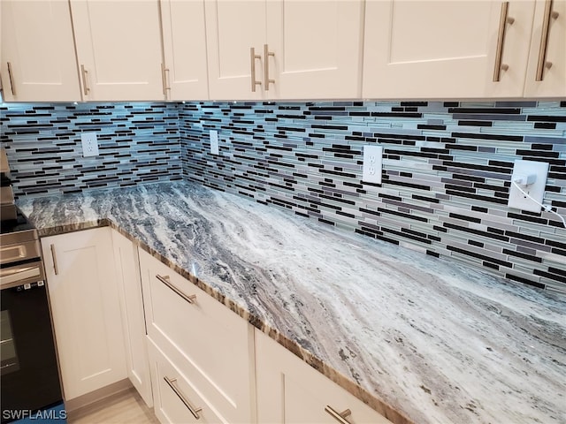 interior details featuring white cabinets, light stone counters, and backsplash