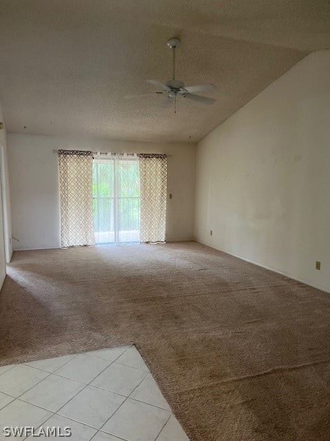 empty room with light tile flooring, vaulted ceiling, ceiling fan, and a textured ceiling