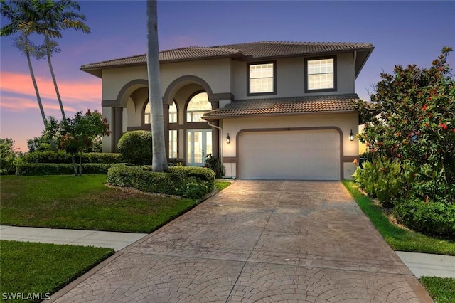 mediterranean / spanish home with a garage, concrete driveway, a lawn, a tiled roof, and stucco siding