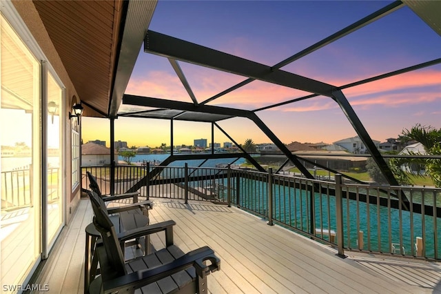 deck at dusk featuring glass enclosure and a water view