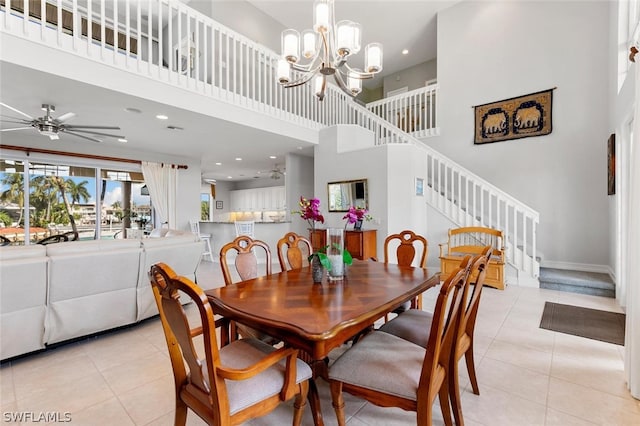 dining area featuring ceiling fan with notable chandelier, light tile patterned flooring, and a high ceiling