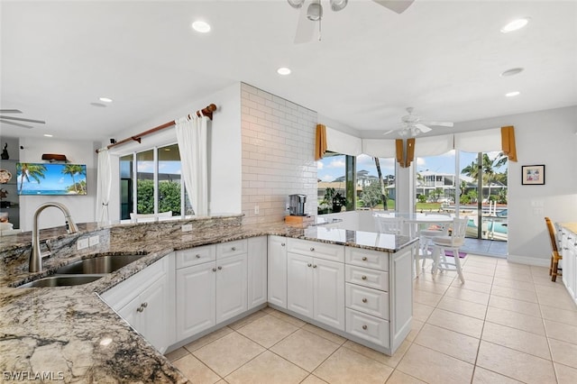 kitchen with white cabinets, light stone countertops, kitchen peninsula, and sink