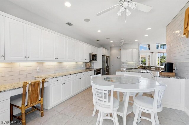 kitchen with white cabinetry, light tile patterned flooring, stainless steel appliances, and light stone counters